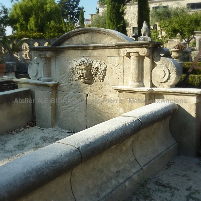 Fontaine murale à long bassin et fronton orné de sculptures en pierre taillée représentant un héros de la mythologie romaine.