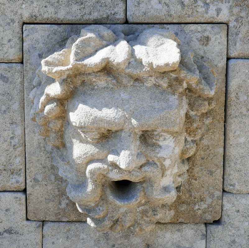 Sortie d'eau en pierre sculptée représentant une tête de Bacchus sur notre fontaine murale