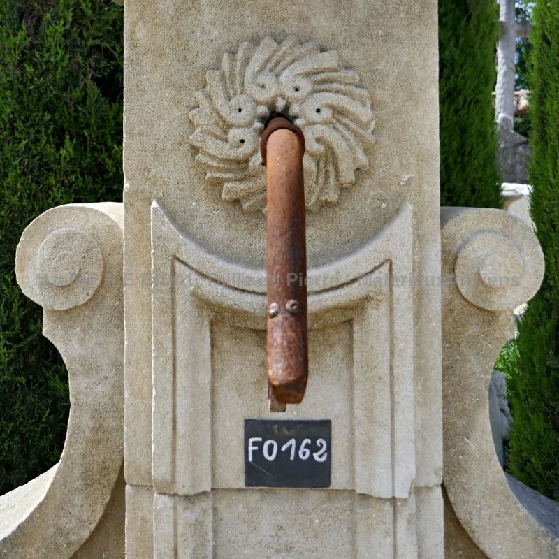 Détail de la sortie d'eau et sculptures en pierre sur le fronton de notre fontaine de jardin en pierre.